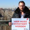 EVG-Bundesjugendsekretär Crispin Kallinger auf der Warschauer Staße in Berlin mit dem Fernsehturm im Hintergrund und Schild: Hier muss investiert werden